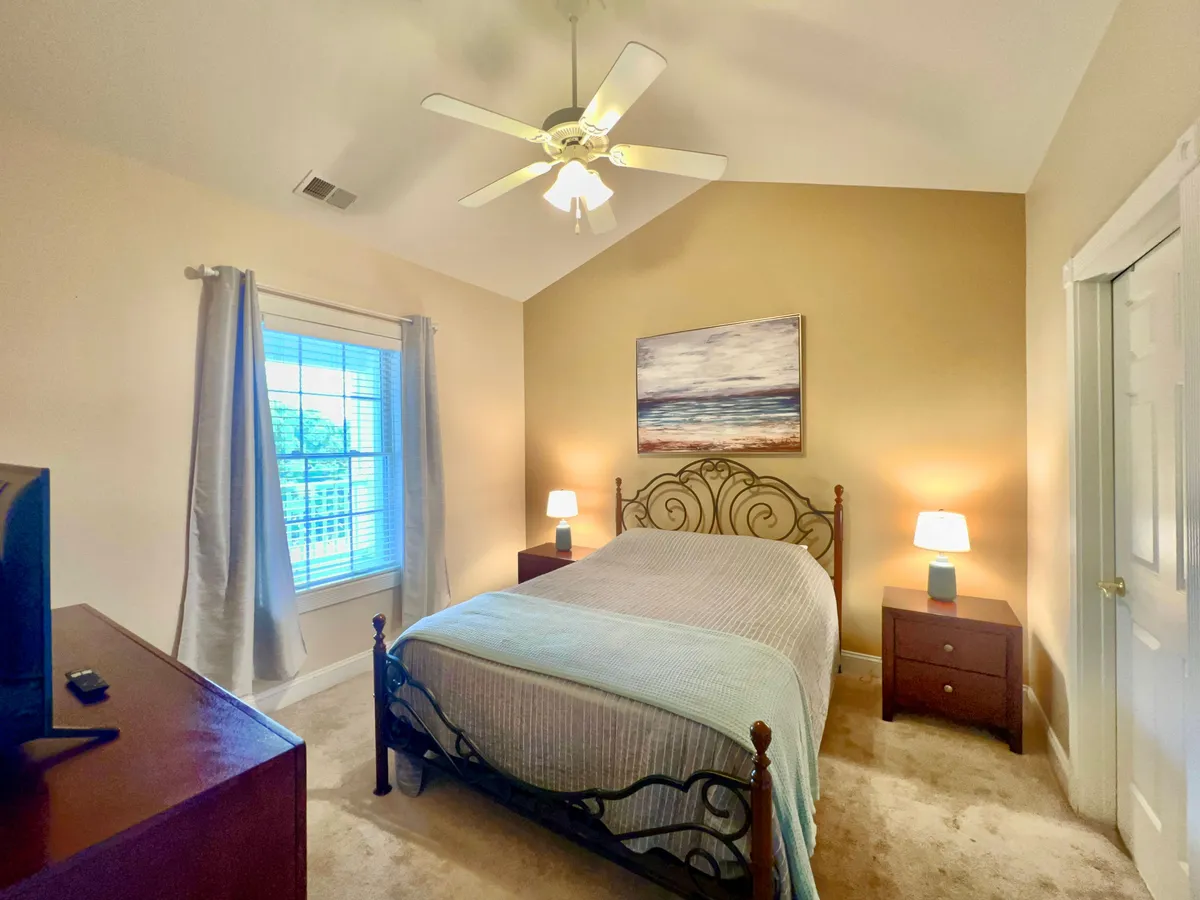 This image shows a serene bedroom featuring a bed with a decorative headboard, soft linens, elegant artwork, and nightstands with lamps. A window with curtains allows natural light to softly illuminate the room, enhancing the calming atmosphere.