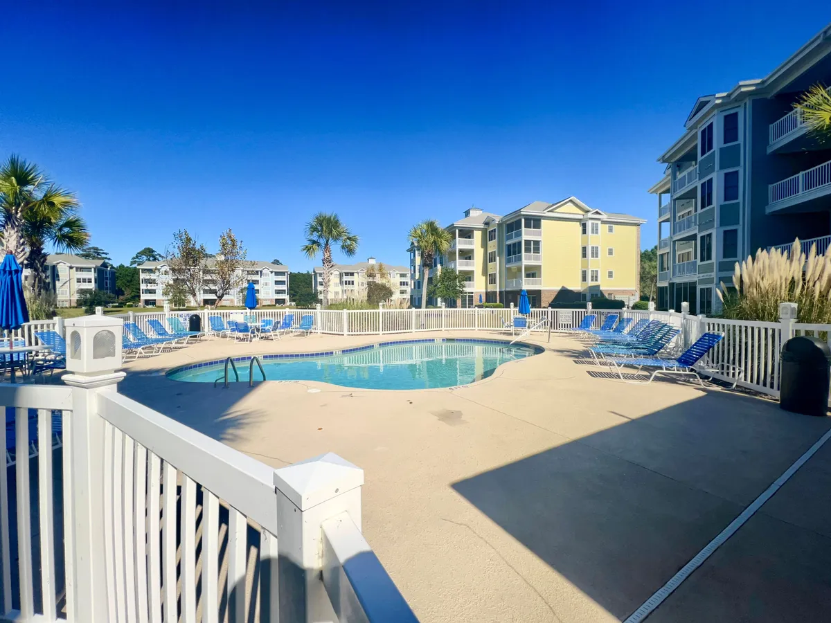 This image showcases a sparkling blue swimming pool surrounded by inviting lounge chairs and swaying palm trees. The scene is framed by the property's residential buildings, evoking a resort-like atmosphere perfect for families to unwind and play together.