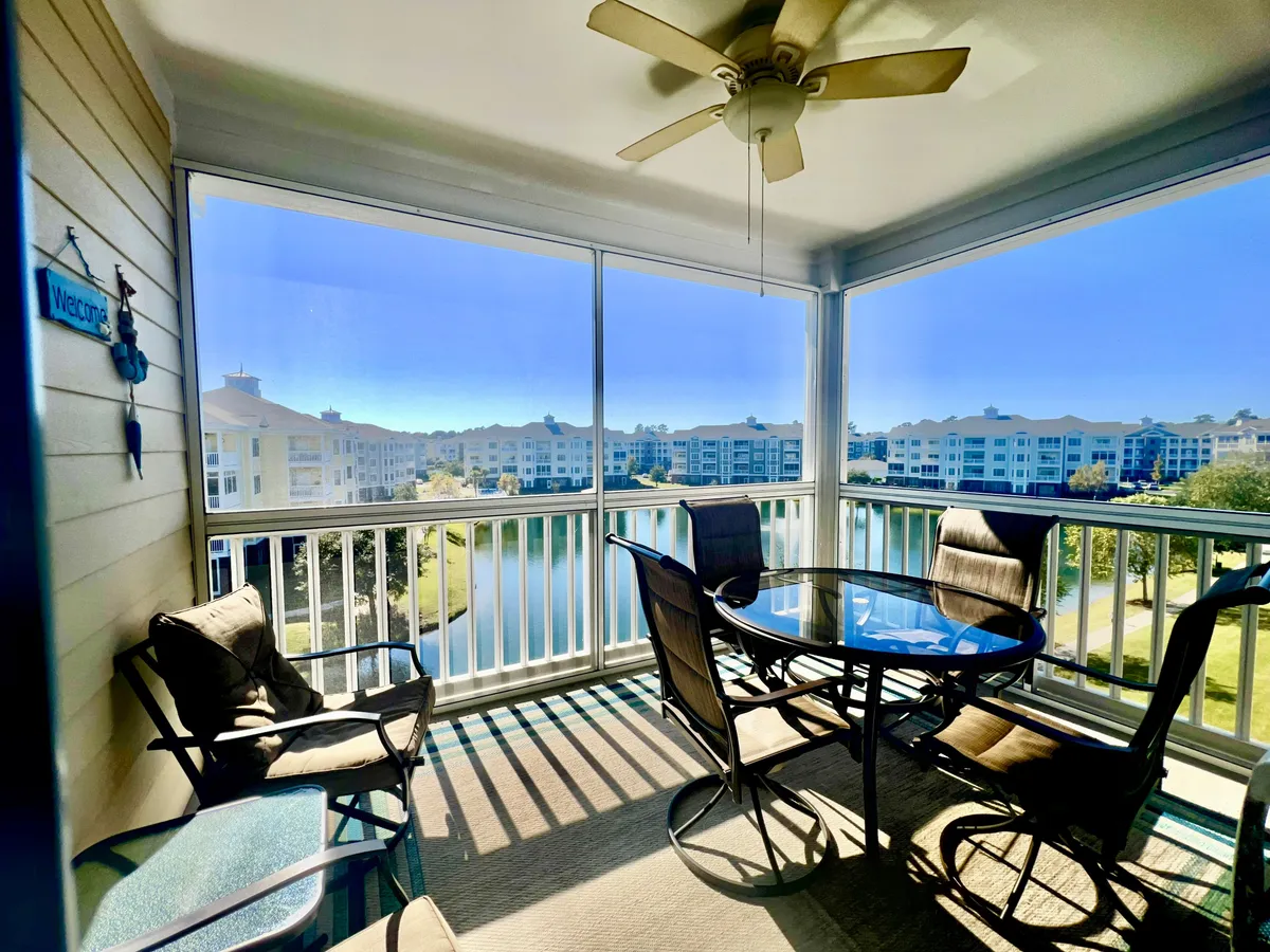 A tranquil screened balcony/veranda with a glass table and comfortable seating, ceiling fan above, and sweeping views over a pond. This airy space is perfect for enjoying morning coffee or relaxing with a book while overlooking the water.