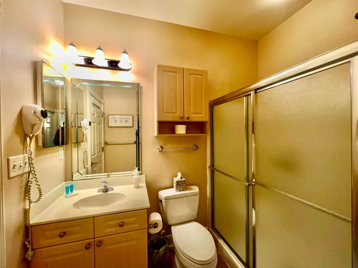 A modern bathroom highlighted by a lit vanity mirror, a glass shower enclosure, and a spacious sink area. The bright, inviting space is ideal for refreshing after a day out.