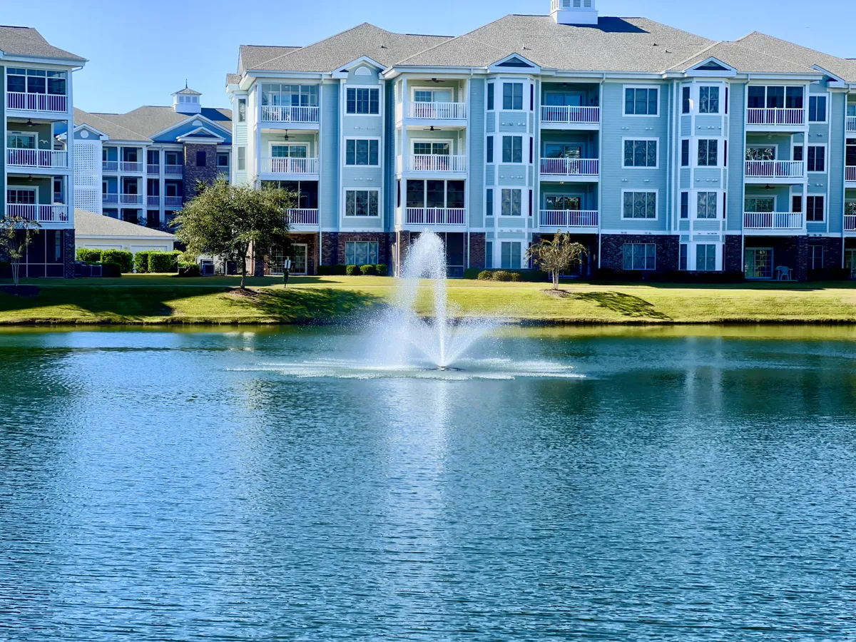 An elegant water fountain set in the middle of a lush green lawn, framed by an apartment building with private balconies. The inviting exterior space promotes relaxation and community engagement.