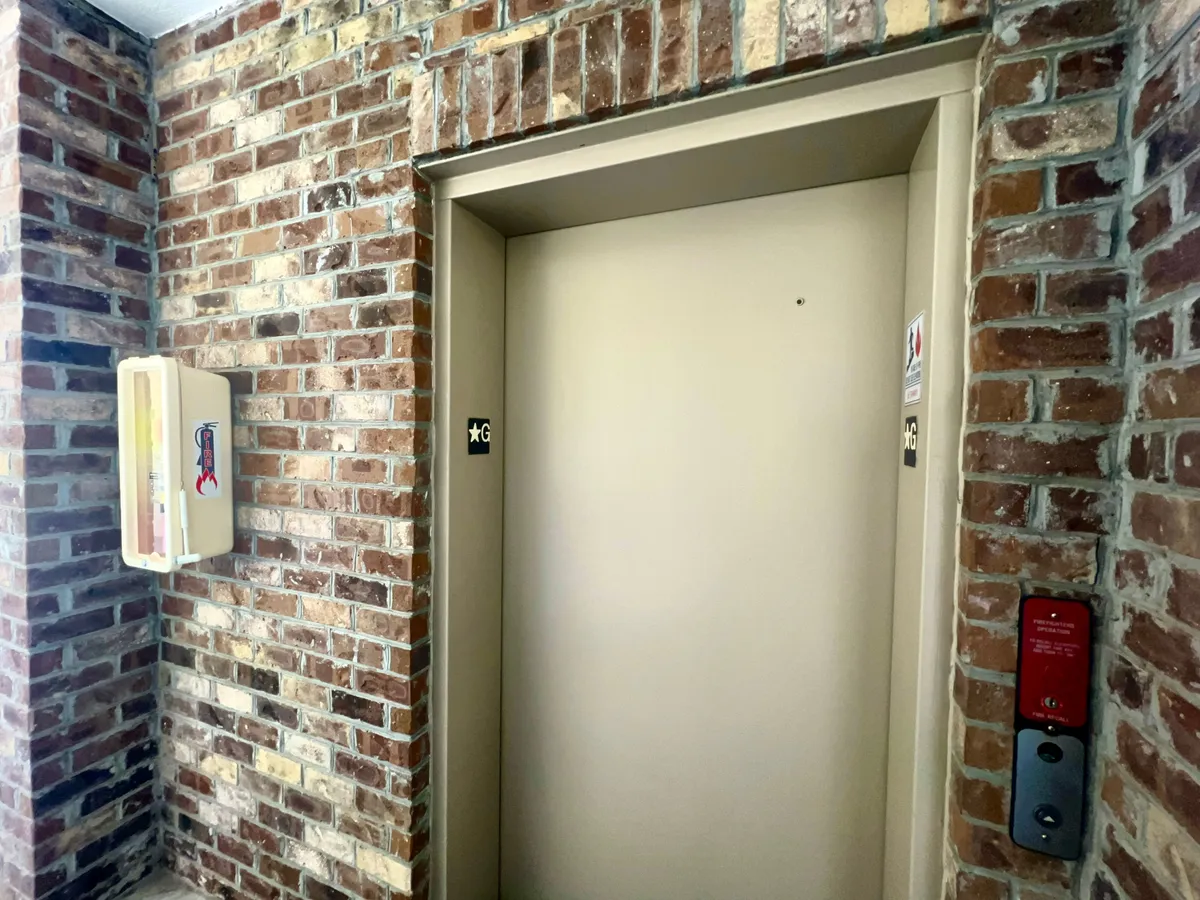 A practical interior corridor view with an elevator door, brick wall details, and a fire extinguisher, conveying convenient access to all floors for guests of all ages.